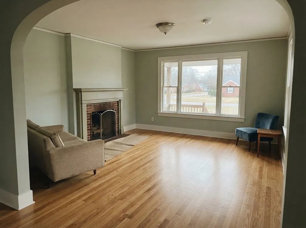 Clean oak living room floor beside a brick fireplace in a 1920s bungalow (hardwood deep cleaning in Hampton, VA)